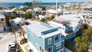 Un edificio de varios pisos con techo plano, cerca de una playa donde se ven barcos y con una vista despejada al océano.