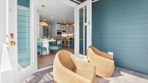 An open patio with wicker furniture, a dining area with a white table and blue chairs, and a kitchen in the background. - Take A Dip- Luxury 6 bedrooms, close to beach, pool and spa!! (Bradenton Beach)