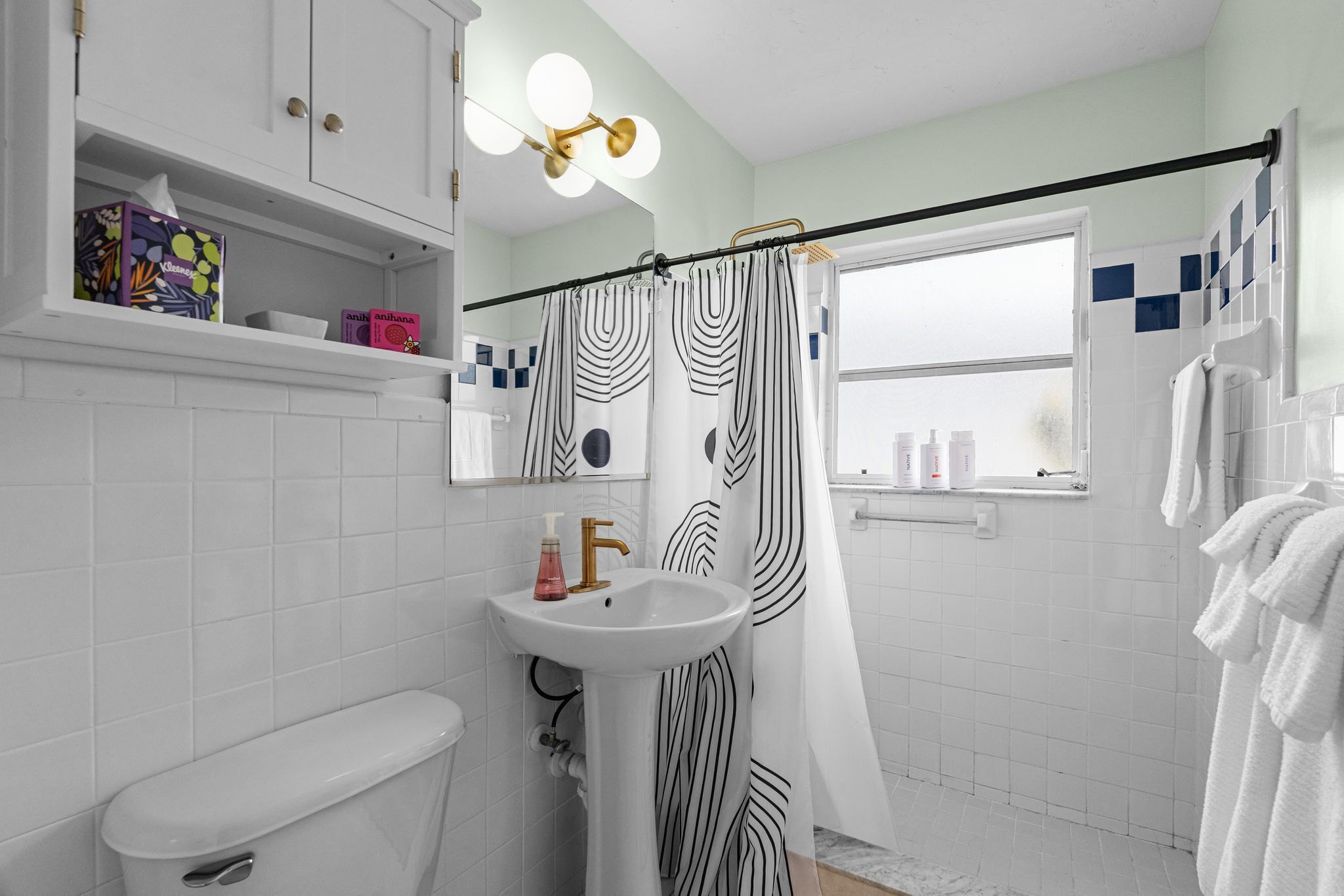 Een badkamer met een witte wastafel, toilet, douchegordijn met zwart-wit patroon en een raam met uitzicht.