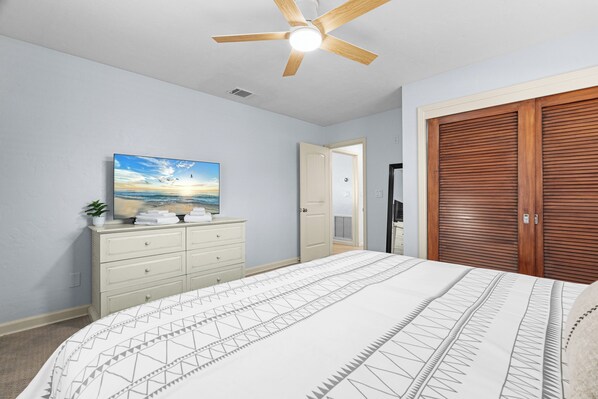 Ein Schlafzimmer mit Bett, Deckenventilator, Kommode, Gemälde und Kleiderschrank.