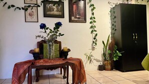 A room with a tiled floor, a wooden table with a patterned tablecloth, a vase with flowers, framed pictures on the wall, and a dark-colored cabinet. - Enchanted Forest (Antigua Guatemala)