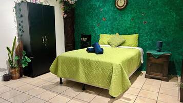 A room with a green textured wall, a bed with green bedding, a clock, and a small table with a lamp.
