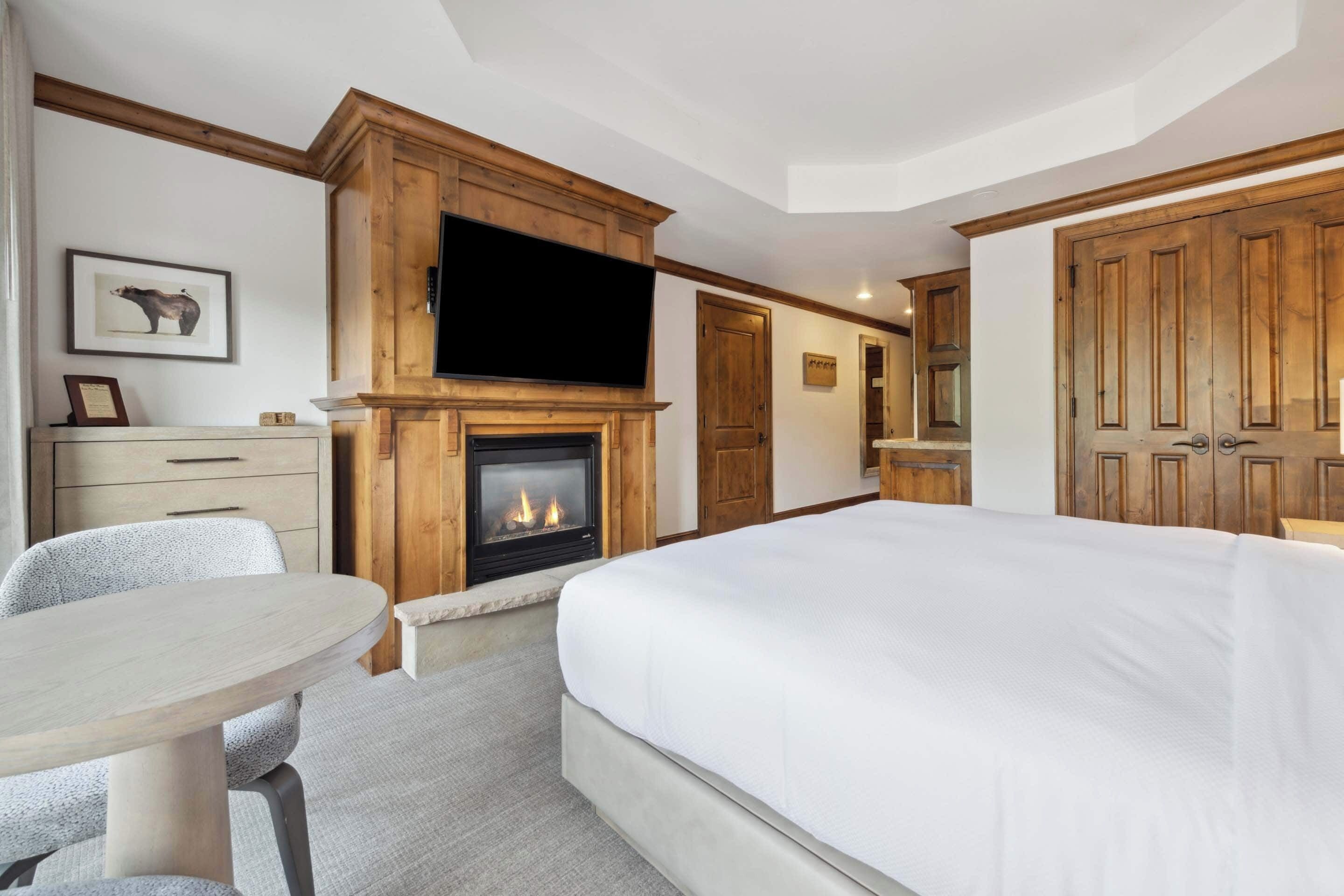 Ett hotellrum med en stor säng, en öppen spis, en tv, ett skrivbord och en stol.