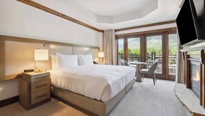 Une chambre d’hôtel dotée d’un grand lit, de tables de chevet, d’un téléviseur à écran plat, d’une cheminée et d’un balcon avec des meubles d’extérieur.