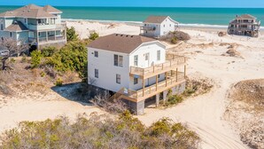 A beachfront property with multiple houses, including a prominent white house with a balcony and a smaller house with a porch. - Semi-oceanfront home on the 4x4 beaches with gorgeous views! (Carova)