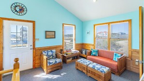 A cozy room with a wooden bench, a sofa, and a small table with books. - Semi-oceanfront home on the 4x4 beaches with gorgeous views! (Carova)