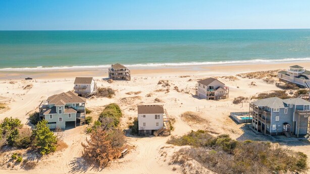A coastal property with multiple houses, some with balconies, situated on sandy terrain with a view of the ocean. - Semi-oceanfront home on the 4x4 beaches with gorgeous views! (Carova)