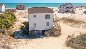A beachfront property with a central white building, a covered deck, and a sandy beach. - Semi-oceanfront home on the 4x4 beaches with gorgeous views! (Carova)