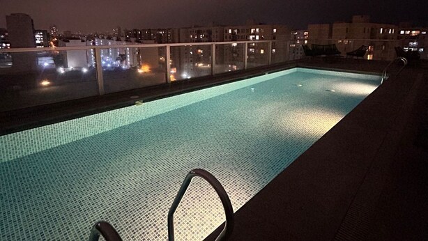 A rooftop swimming pool with a glass balustrade, surrounded by city buildings at night. - Beautiful Apartment in Lima (Lima)