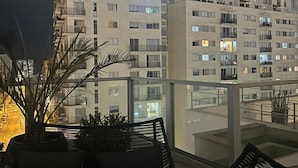A balcony with a sofa and potted plants, overlooking a high-rise building with multiple balconies and windows. - Beautiful Apartment in Lima (Lima)