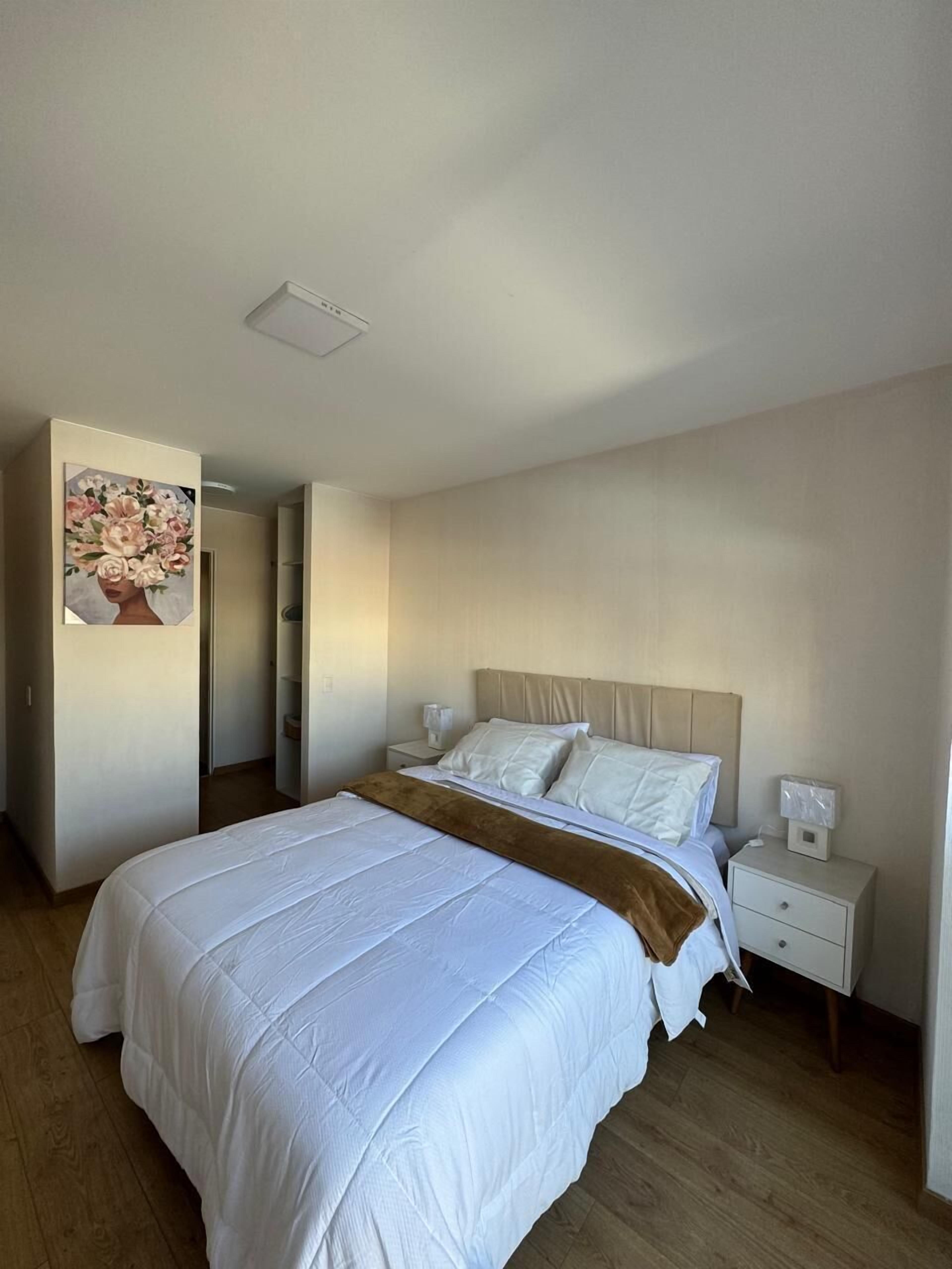 A bedroom with a large bed, a nightstand, a bedside table, and a painting on the wall.