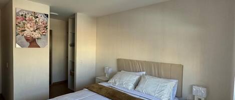 A bedroom with a large bed, a nightstand, a bedside table, and a painting on the wall.