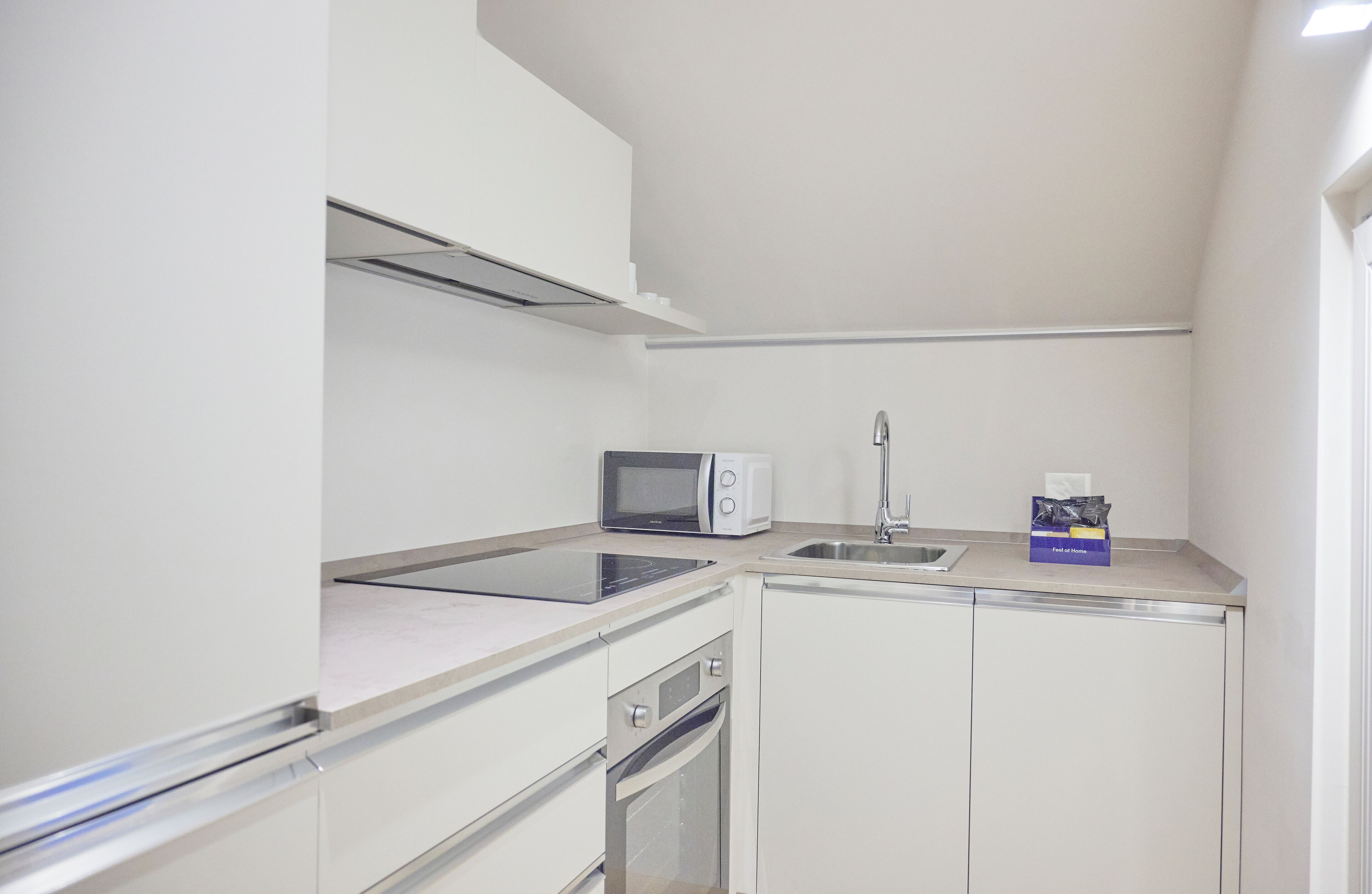 A compact kitchenette with a microwave, toaster, sink, and a dish rack.