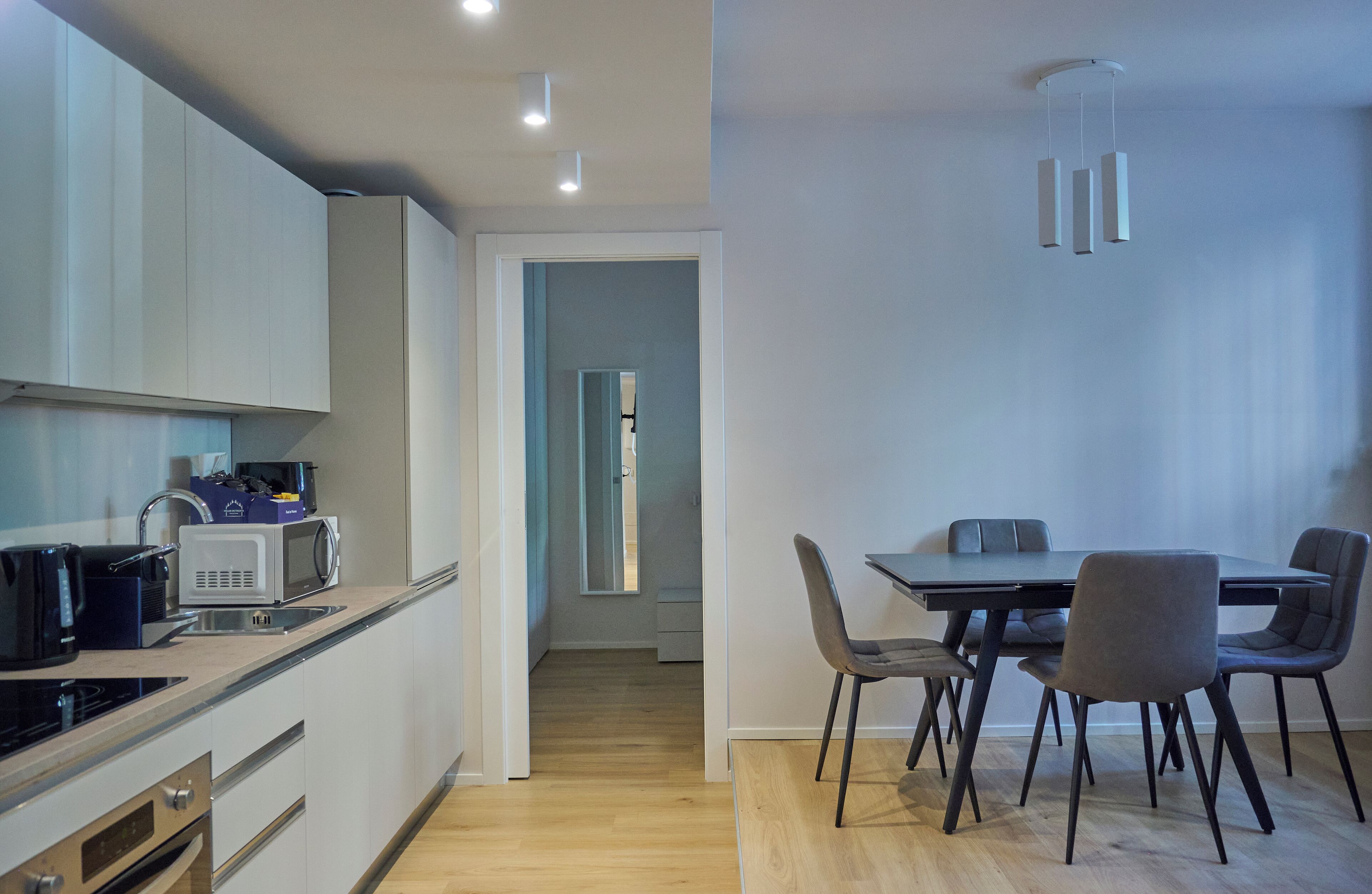 Een moderne keuken met een magnetron, broodrooster en spoelbak. Er is een eethoek met een tafel en stoelen.