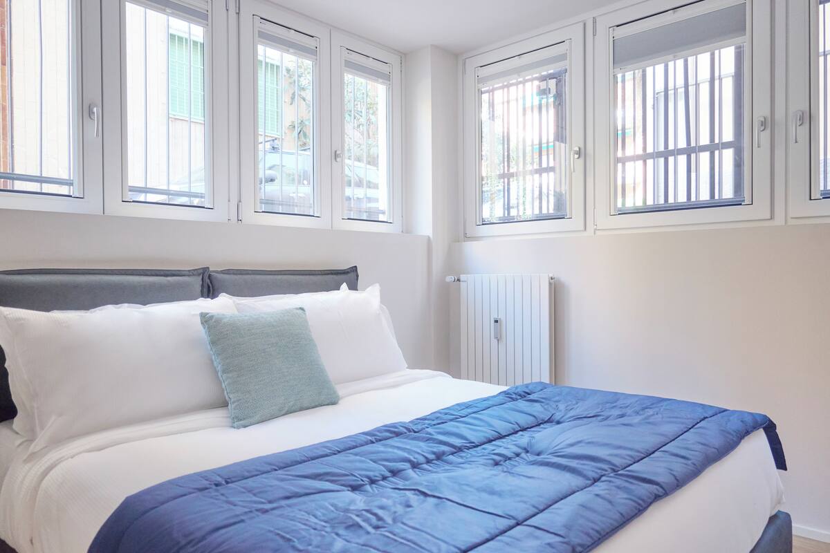 Une chambre à coucher avec un lit, des murs blancs et des fenêtres avec des barreaux.