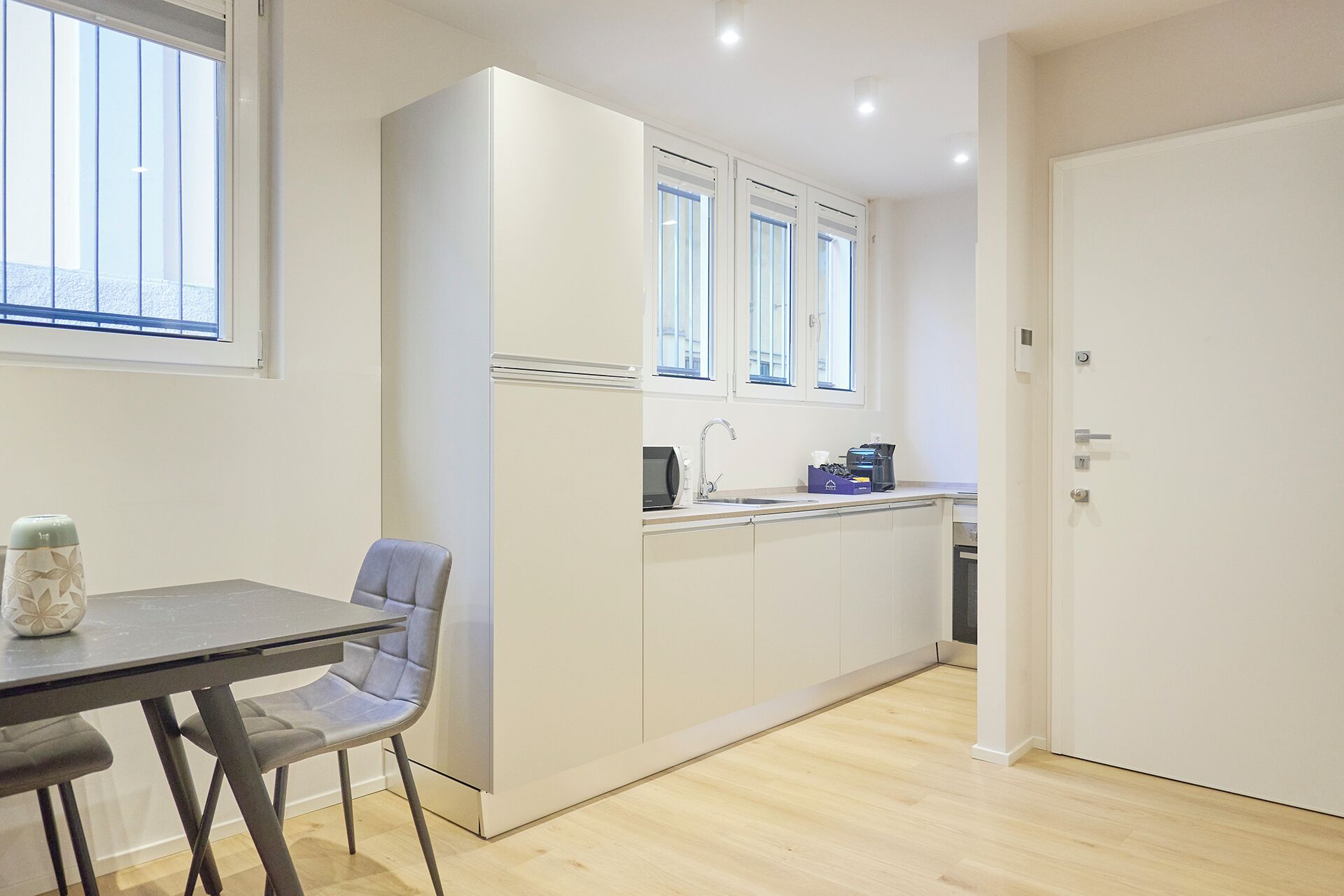Cocina compacta con comedor, microondas, cafetera y un armario con ventana sobre el fregadero.