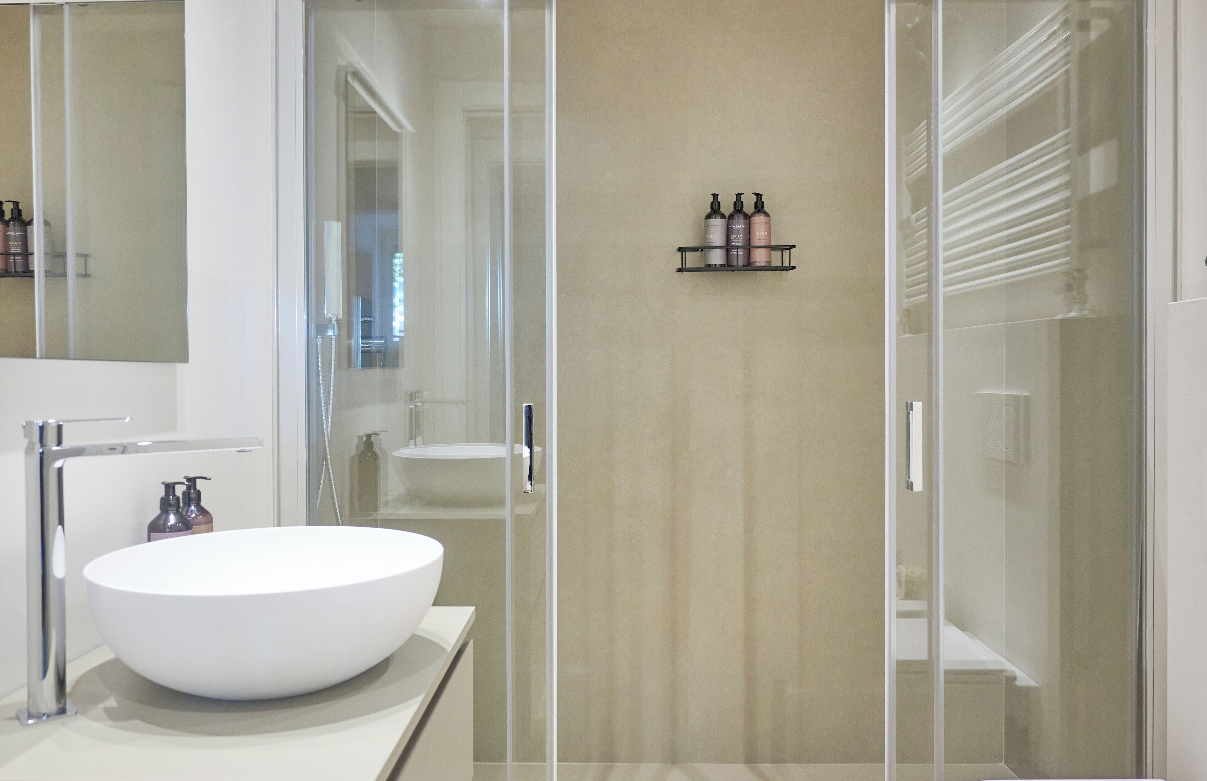 Ein modernes Badezimmer mit einem großen, weißen Waschbecken, einer Duschkabine aus Glas und einem Ablagebereich für Pflegeprodukte.