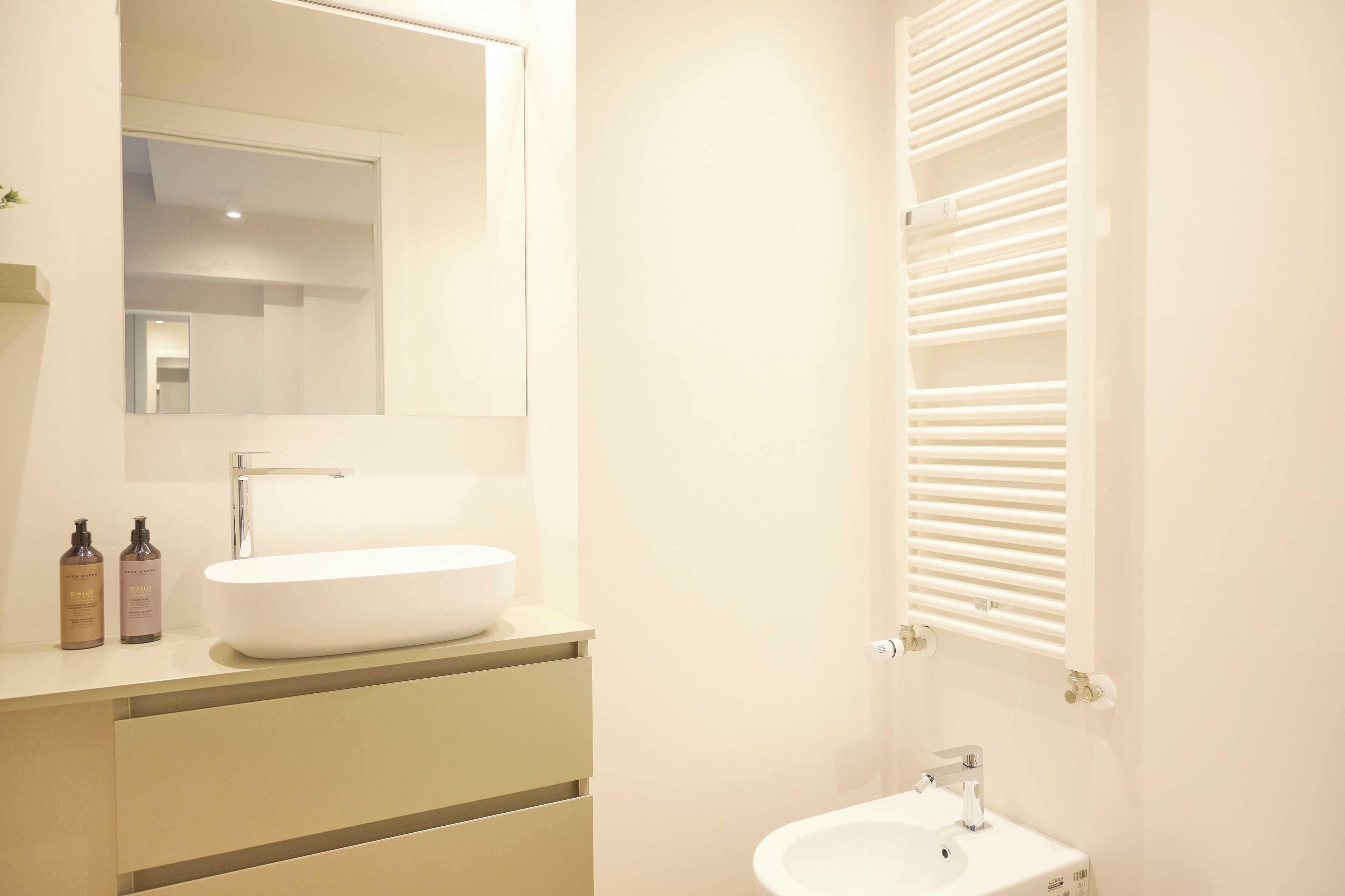 A modern bathroom with a large mirror, a white sink, and a built-in heater.