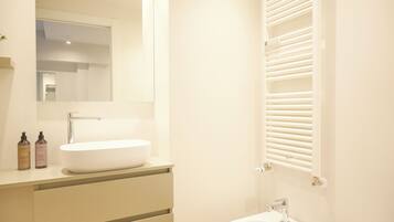 A modern bathroom with a large mirror, a white sink, and a built-in heater.