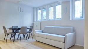 Un salon moderne avec un canapé blanc, une table à manger avec des chaises et de grandes fenêtres.