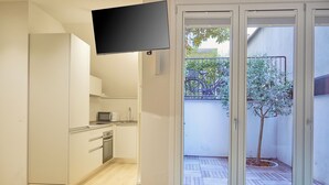 Une cuisine moderne équipée d’un téléviseur à écran plat, d’un petit coin repas et d’une porte-fenêtre coulissante donnant sur un balcon avec un arbre.