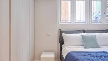 A bedroom with a bed, a nightstand, and a window with blinds.