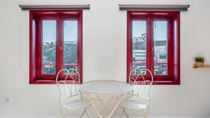 A room with two red-framed windows, a round table with four chairs, and a small plant on a shelf. - GuestReady - Oporto Old Town House 3 (Porto)