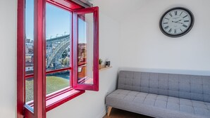 A room with a grey sofa, a red-framed window, and a wall clock. - GuestReady - Oporto Old Town House 3 (Porto)