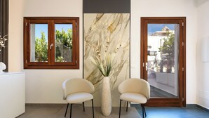 Un área de recepción con dos sillones, un arte mural de mármol y un ventanal con marco de madera.