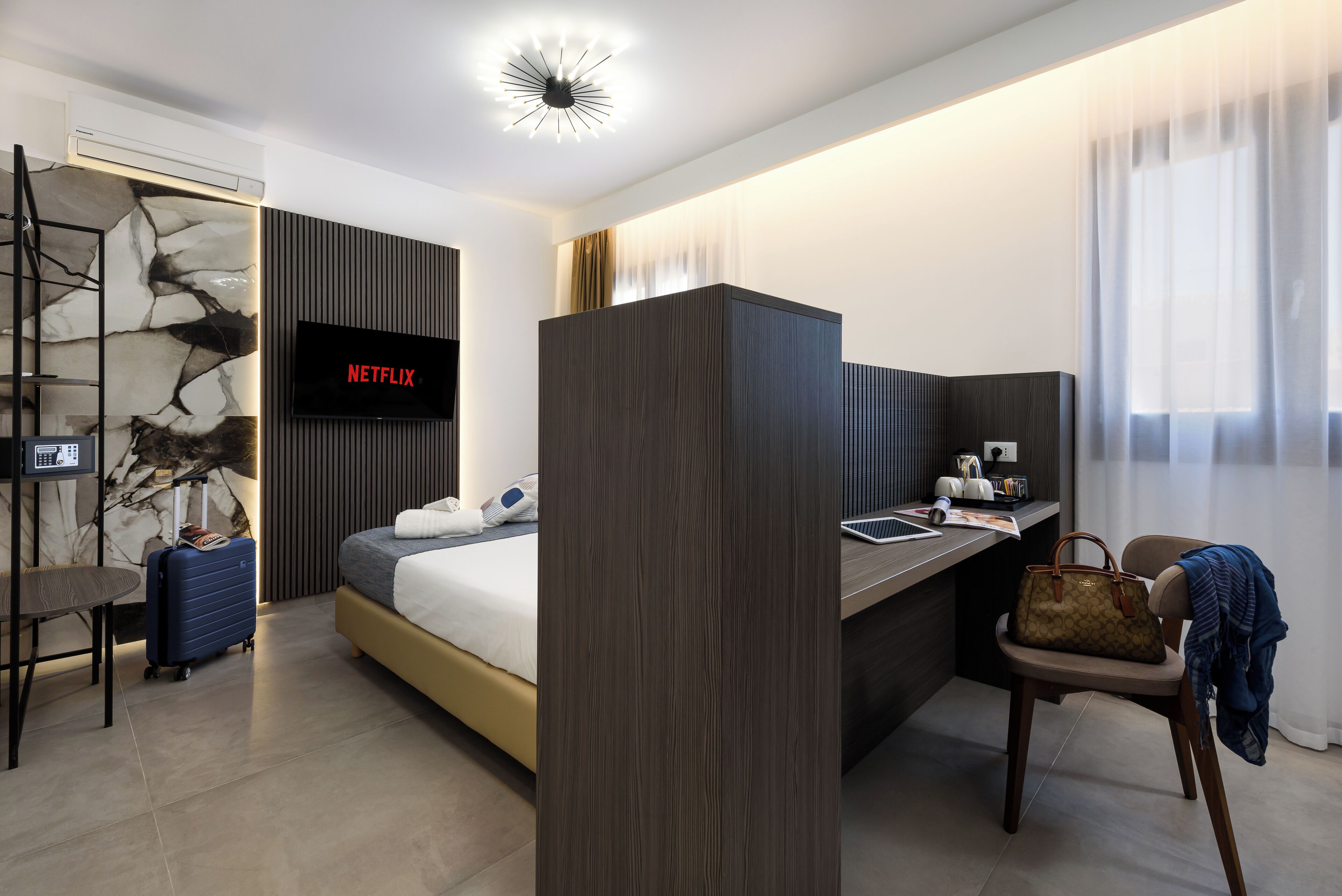 A modern hotel room with a bed, desk, chair, and a TV displaying 'NETFLIX'.