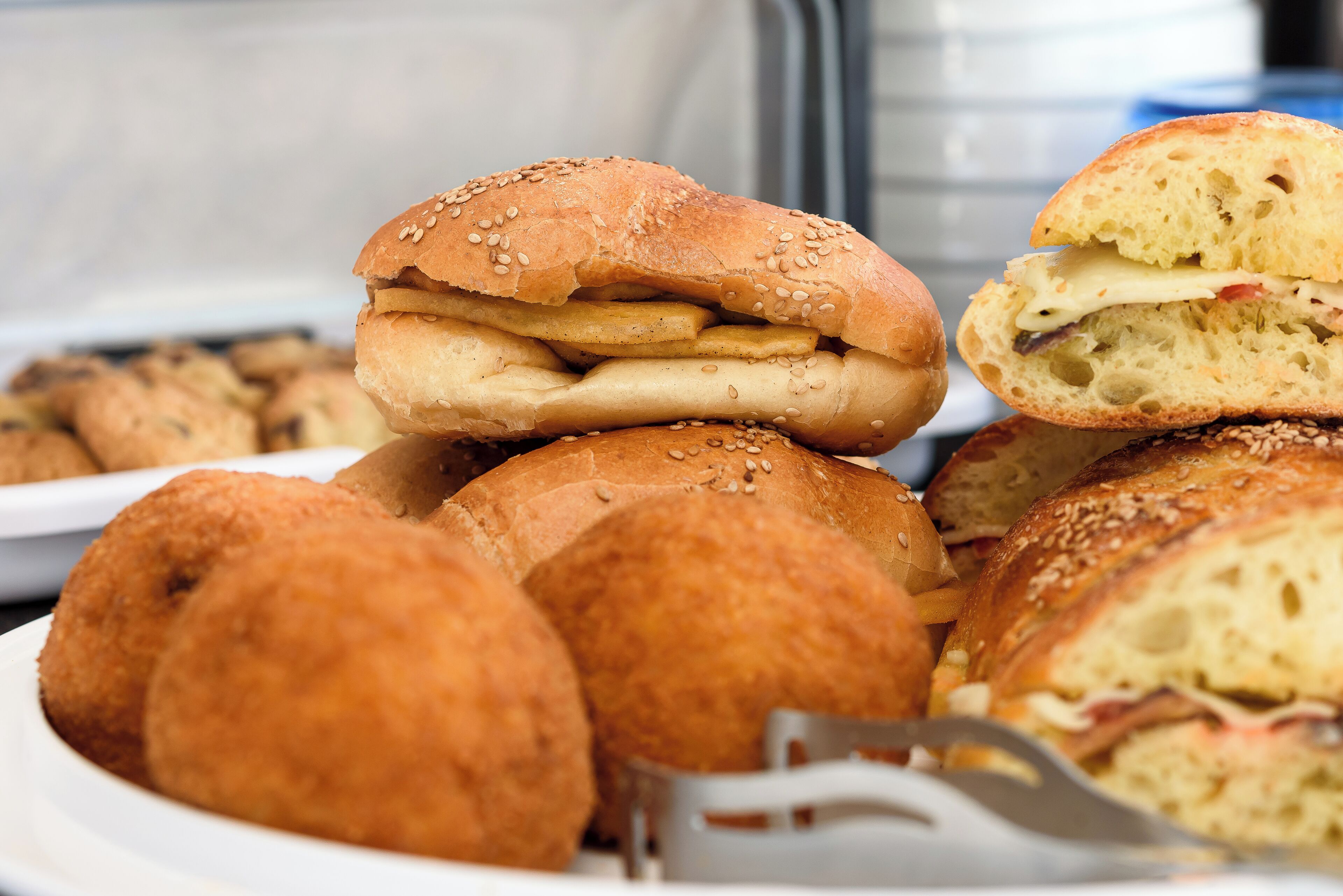 A plate of sandwiches and rolls, including a sandwich with cheese and ham, and a roll with sesame seeds.