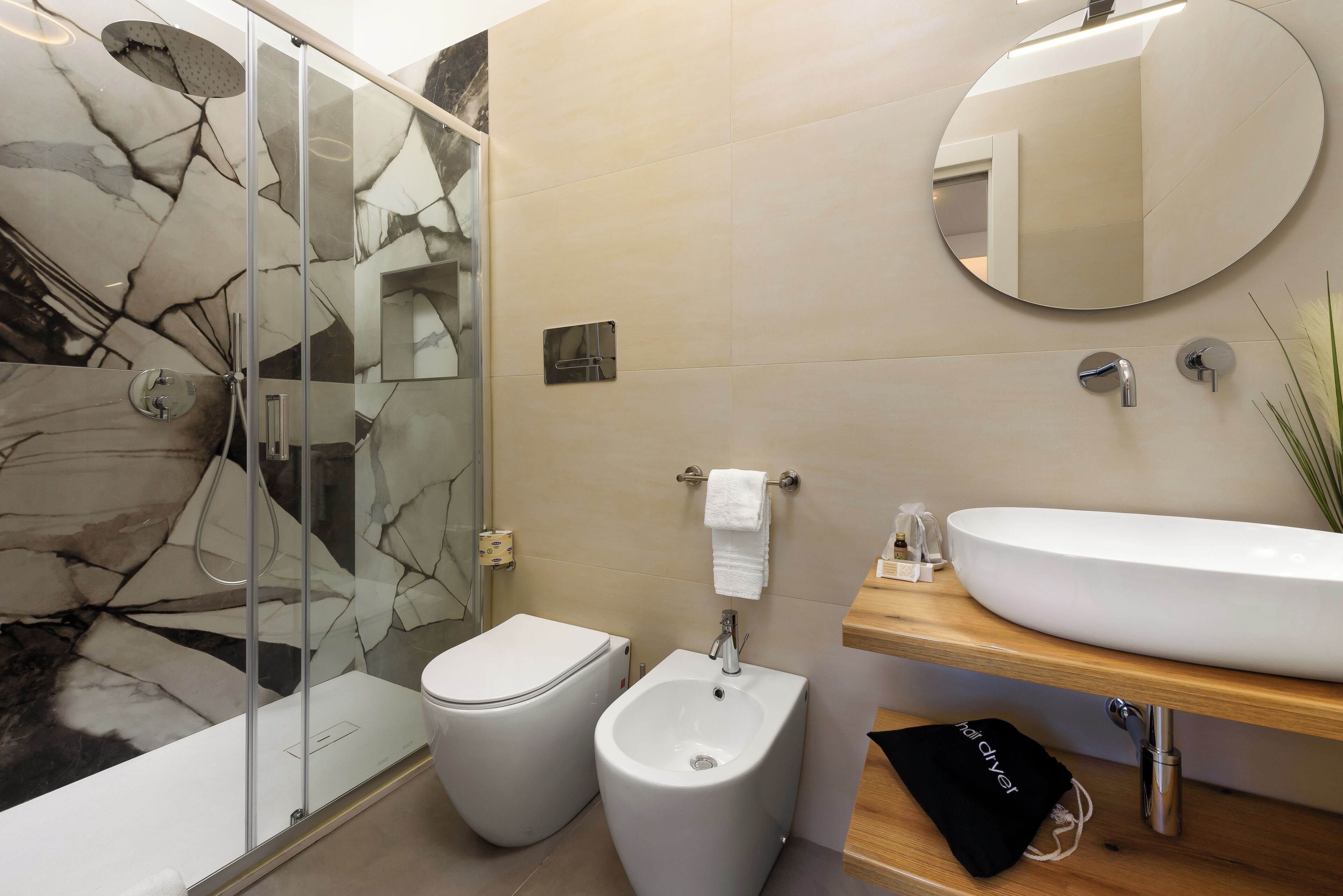 Une salle de bain moderne avec une douche à parois de verre, un bidet, des toilettes, un lavabo avec un miroir et un porte-serviettes.