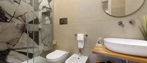 Une salle de bain moderne avec une douche à parois de verre, un bidet, des toilettes, un lavabo avec un miroir et un porte-serviettes.