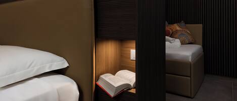 A bedroom with a bed, a reading nook with a chair and a book, and a small table with a lamp.