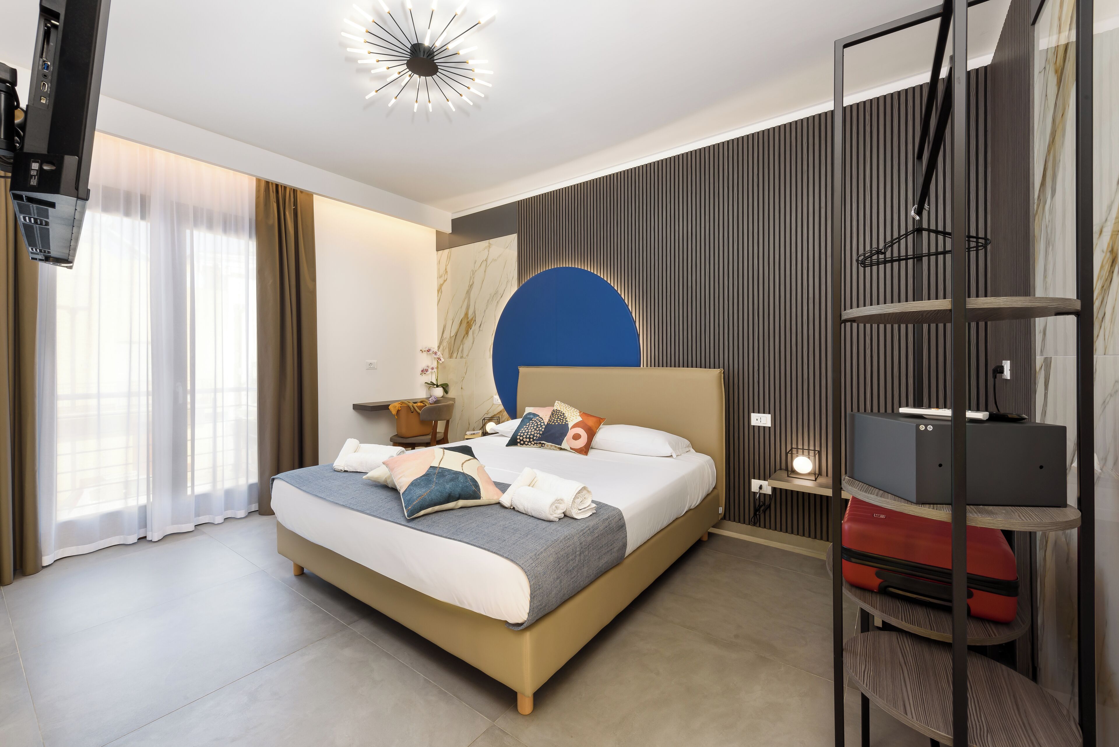 Una habitació d'hotel moderna amb un llit gran, televisió, escriptori amb làmpada i un armari.