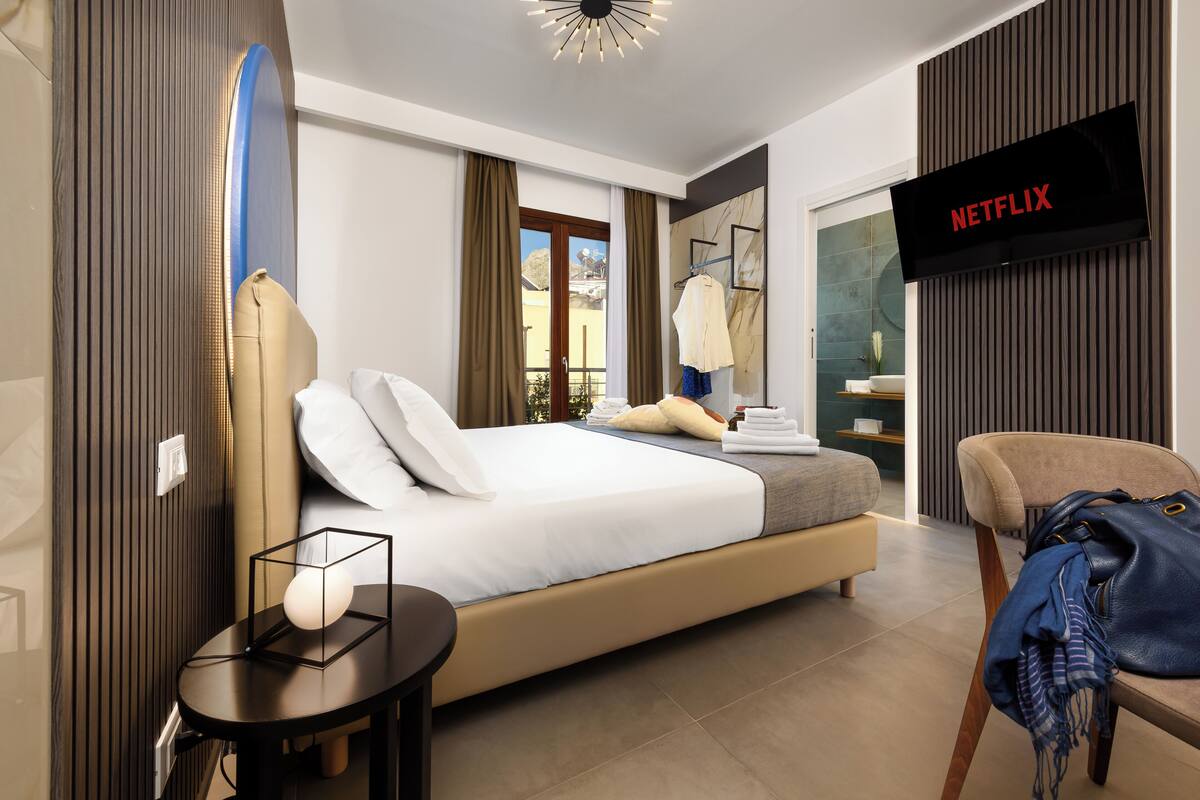A modern hotel room with a large bed, a TV mounted on the wall, and a view of the outdoors.