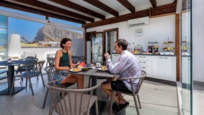 A dining area with a table and chairs, a kitchen in the background, and a view of a mountain. - Bedda Luna B&B (San Vito Lo Capo)