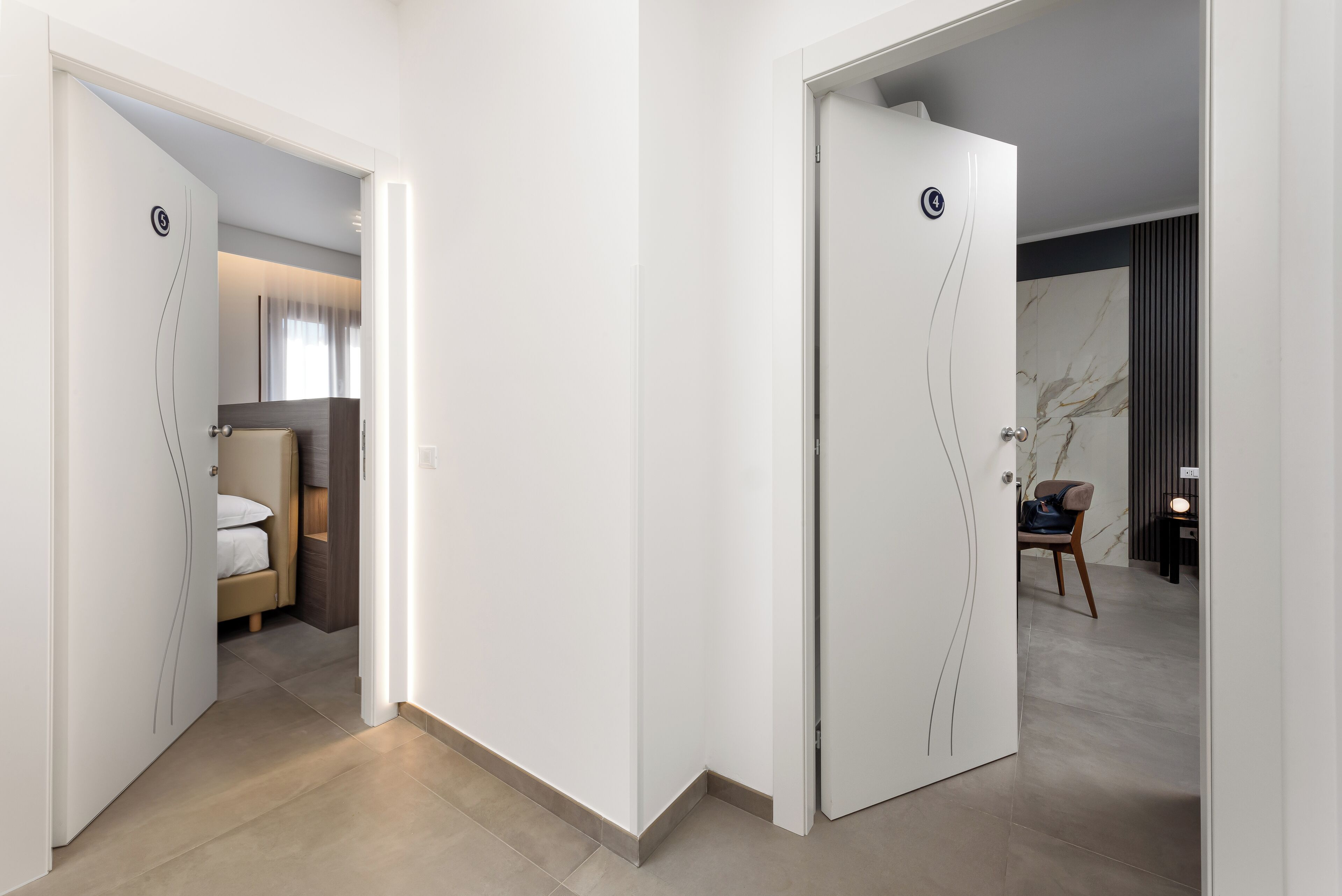 Een hotelgang met witte deuren, een bed en een stoel.