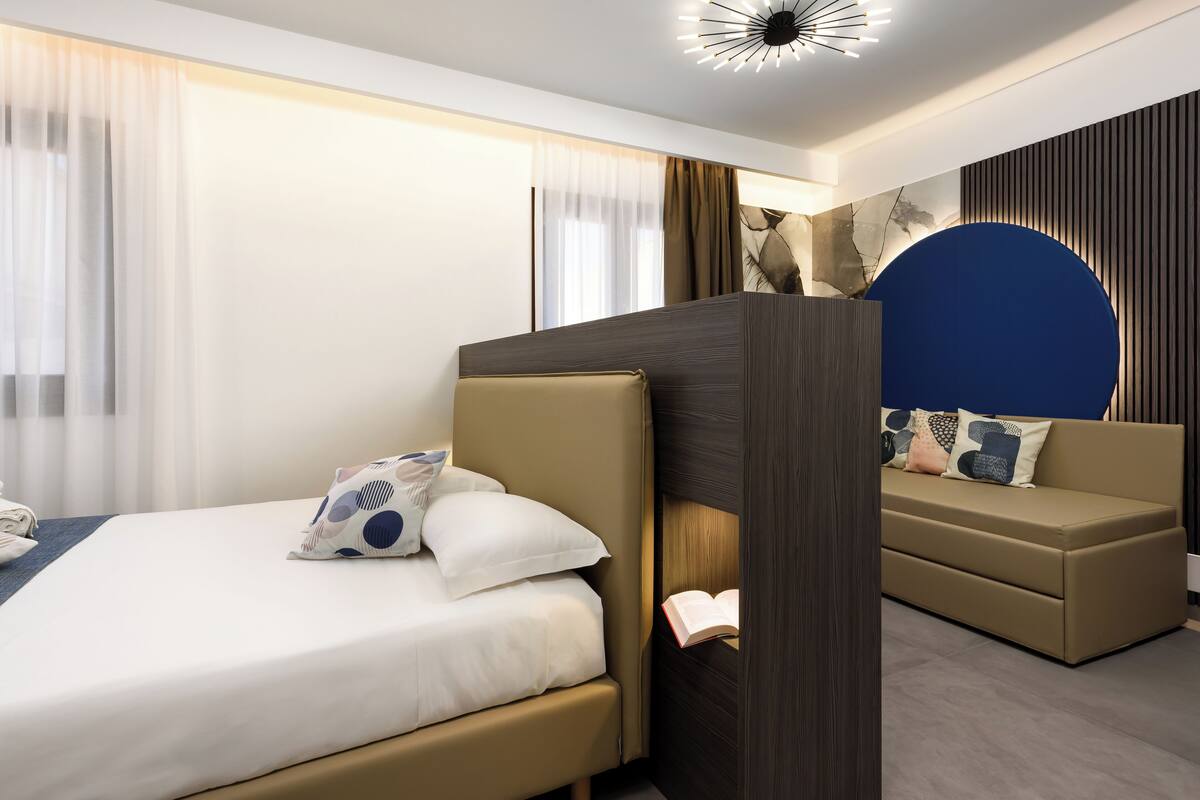 A modern hotel room with a bed, a sofa, and a large blue accent wall.