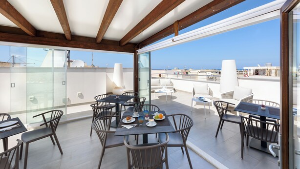 Una terraza en la azotea con zona de comedor, mesas y sillas, y vistas despejadas del horizonte de la ciudad.