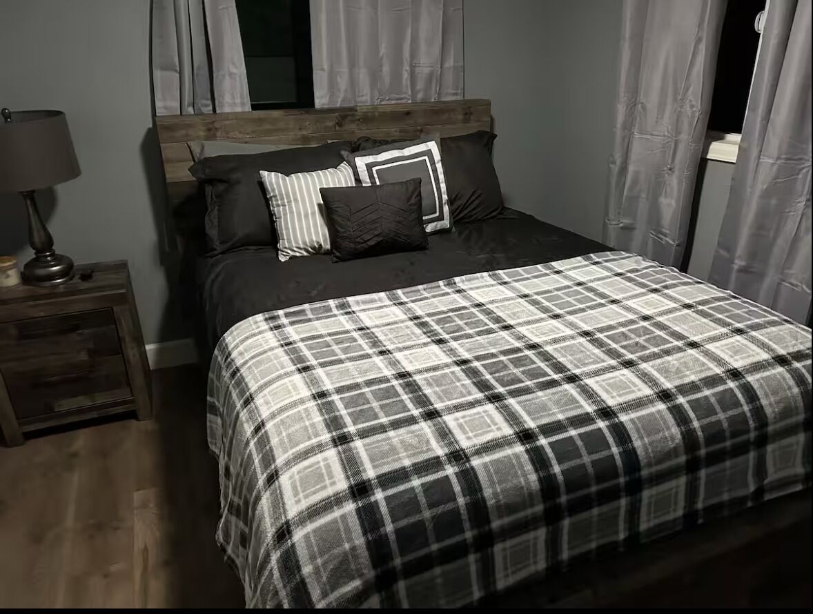 Een slaapkamer met een houten hoofdeinde, een zwart-wit geruit beddegoed en een nachtkastje met een lamp.