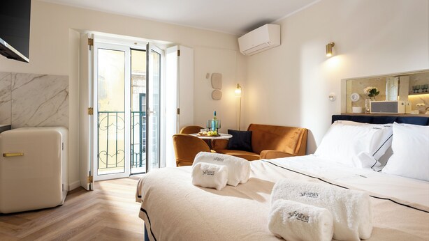 A hotel room with a bed, a seating area with a table, a refrigerator, and a balcony with a view. - Saudade Center Alfama II (Lisbon)