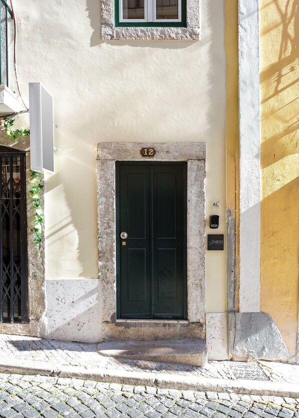 A building with a dark green door, a number '12' above it, and a small sign on the right. - Saudade Center Alfama II (Lisbon)
