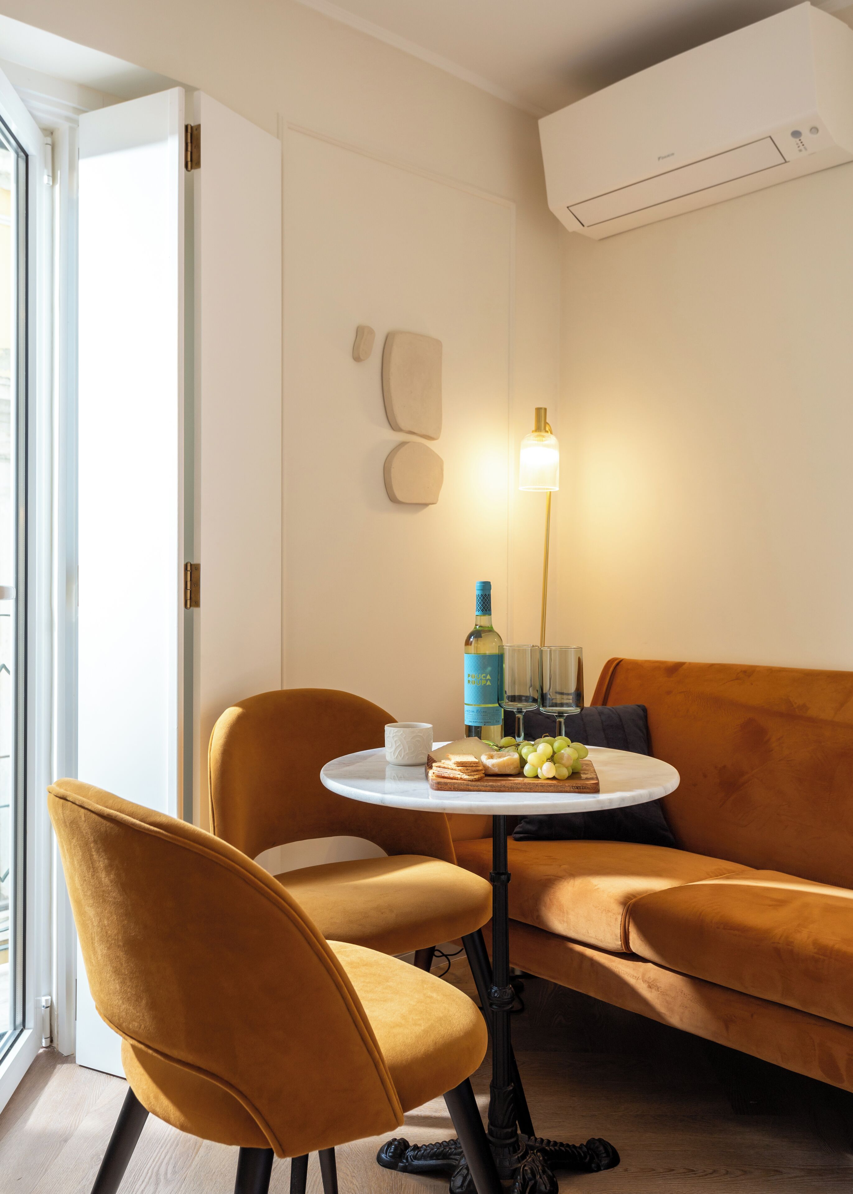 A modern room with a round table, two chairs, a sofa, and a wall-mounted air conditioner.