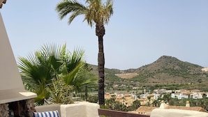 Eine Terrassenanlage im Freien mit einem runden Tisch und gestreiften Stühlen, mit Blick auf einen Hügel mit Gebäuden.