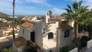 Ein weißes Gebäude mit einem Ziegeldach, einem kleinen Balkon und Blick auf eine Küstenstadt.