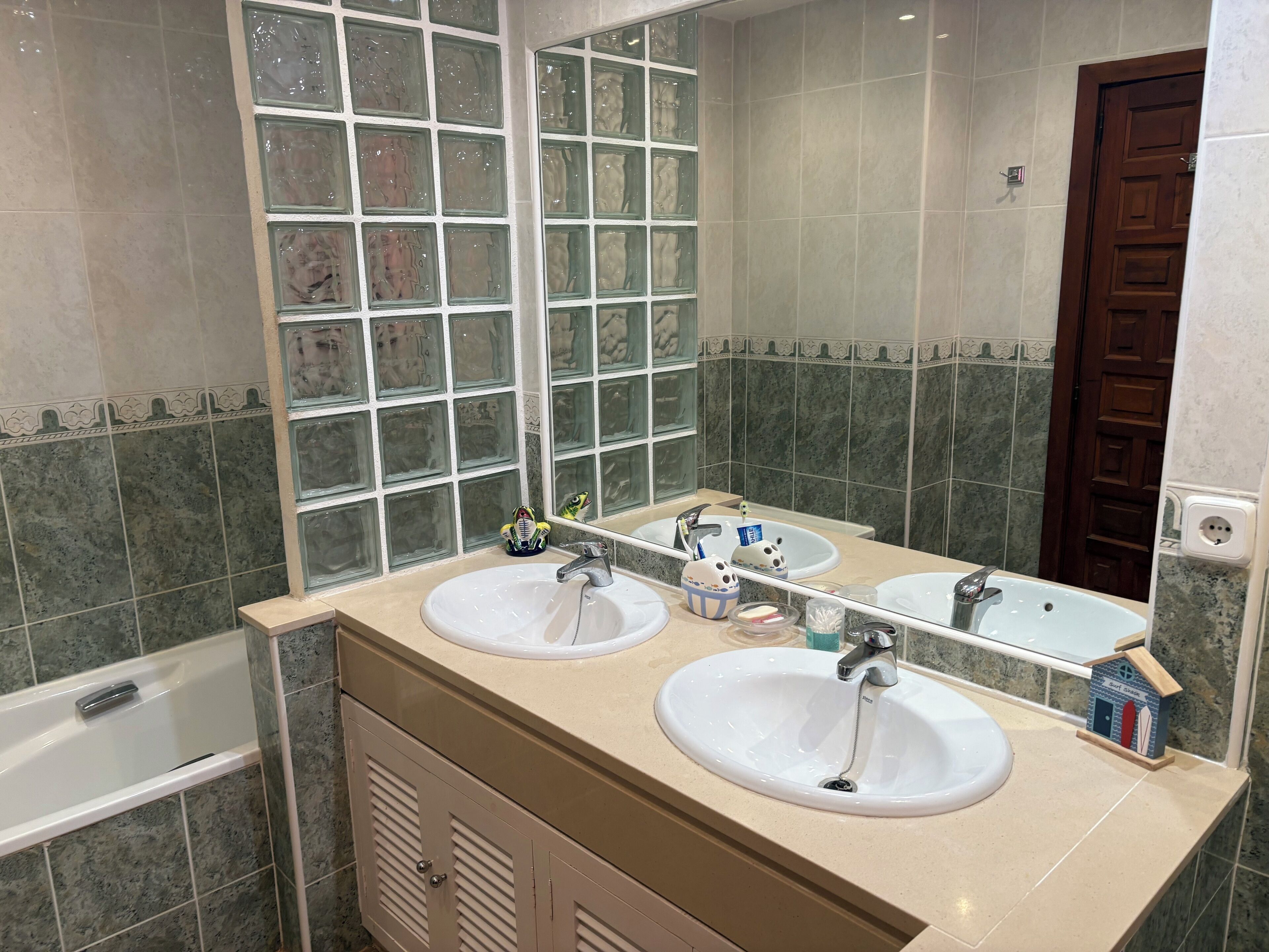 Un baño con dos lavamanos, un espejo y una ventana con bloques de vidrio decorativos.