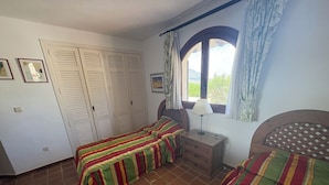 Ein Schlafzimmer mit zwei Betten, einem Fenster mit Vorhängen, einem Nachttisch mit Lampe und einem Kleiderschrank.
