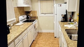 A compact kitchen with white cabinets, a granite countertop, a built-in oven, and a window with blinds. - Charming 2-bedroom estate in beautiful Williamsburg with WiFi, fitness room (Williamsburg)