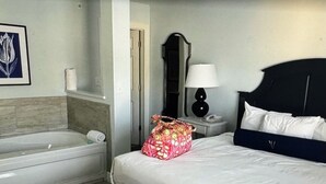 A hotel room with a large bed, a bedside table with a lamp, a bathroom with a bathtub, and a mirror. - Charming 2-bedroom estate in beautiful Williamsburg with WiFi, fitness room (Williamsburg)